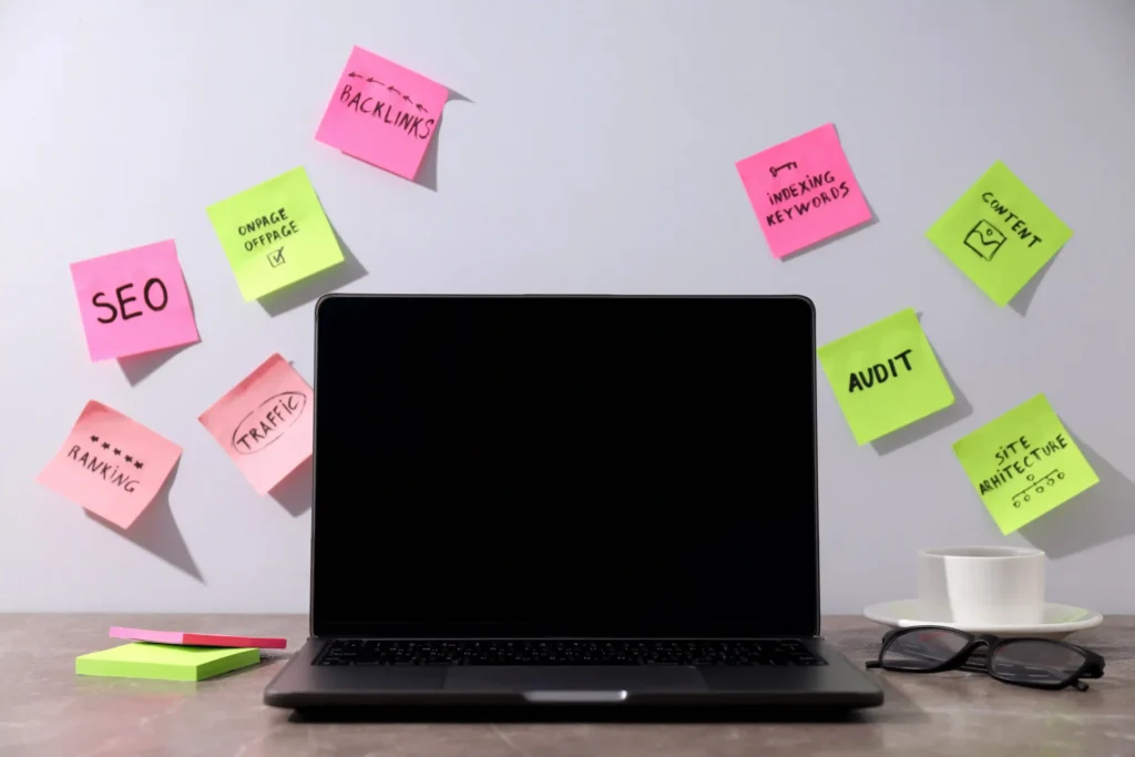 Sticky notes with SEO terms on a wall behind a laptop and glasses, representing elements of technical SEO work.