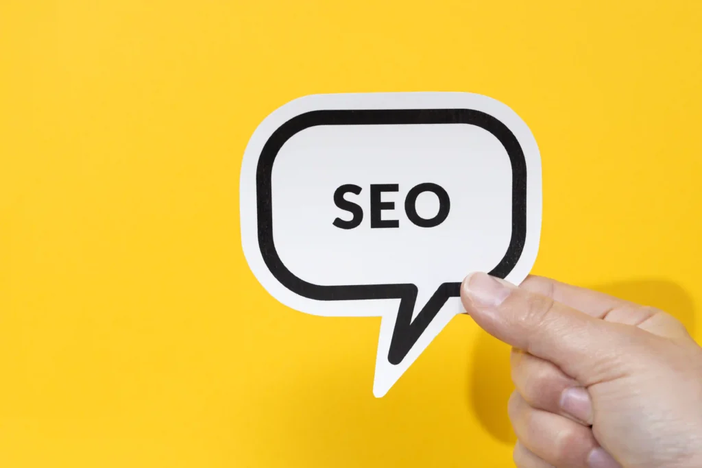 Hand holding a speech bubble with the word SEO, representing the importance of keywords in on page SEO content writing.