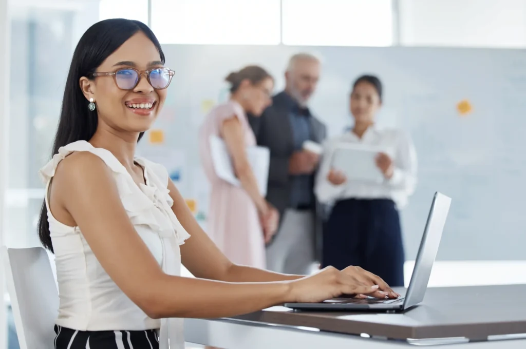 Professional woman smiling while working on a laptop in an office, portraying a content writer engaged in on page SEO content writing.