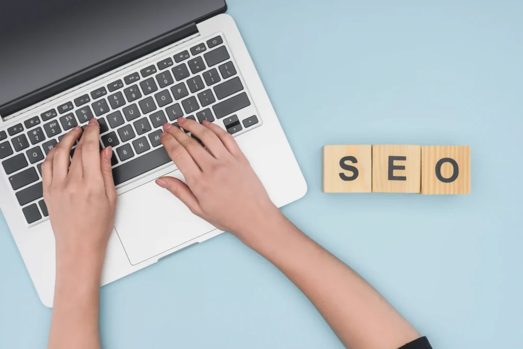 Hands typing on a laptop next to wooden SEO blocks representing on page SEO keyword research work