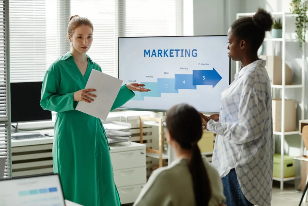 Woman presenting a marketing strategy to colleagues, highlighting the role of planning and research in applying marketing psychology studies.