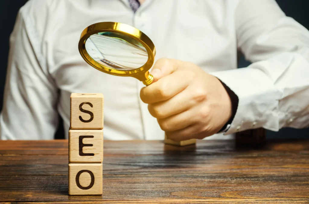 Person examining wooden SEO blocks with magnifying glass, representing analysis of SEO link building websites
