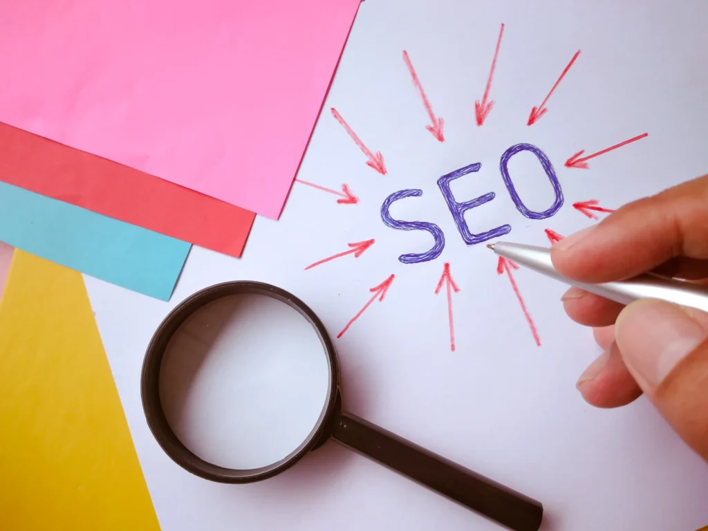 Hand-drawn SEO text with red arrows and colorful paper background representing the concept that SEO help business visibility.