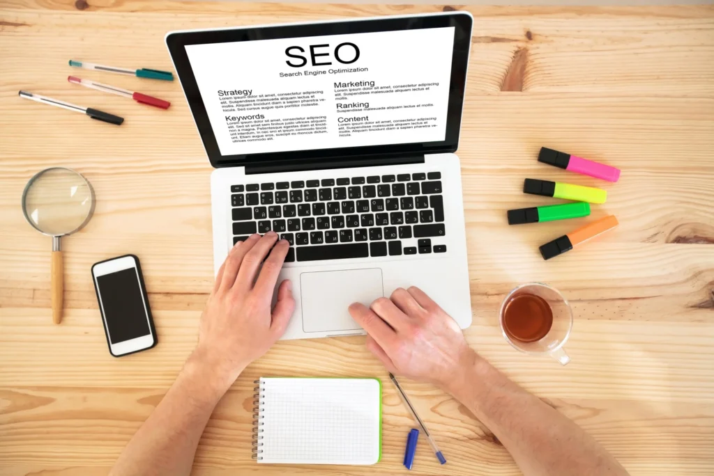 Overhead view of a marketer working on an seo services template using a laptop with SEO terms displayed.