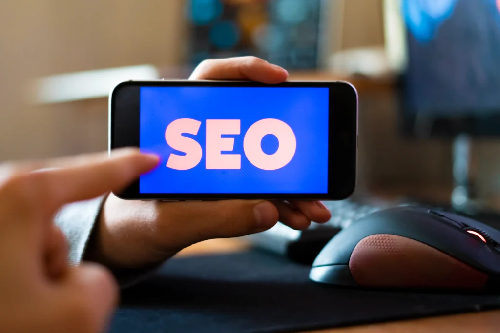 Close-up of man holding smartphone with bold SEO text, symbolizing how SEO help business build digital presence on mobile.