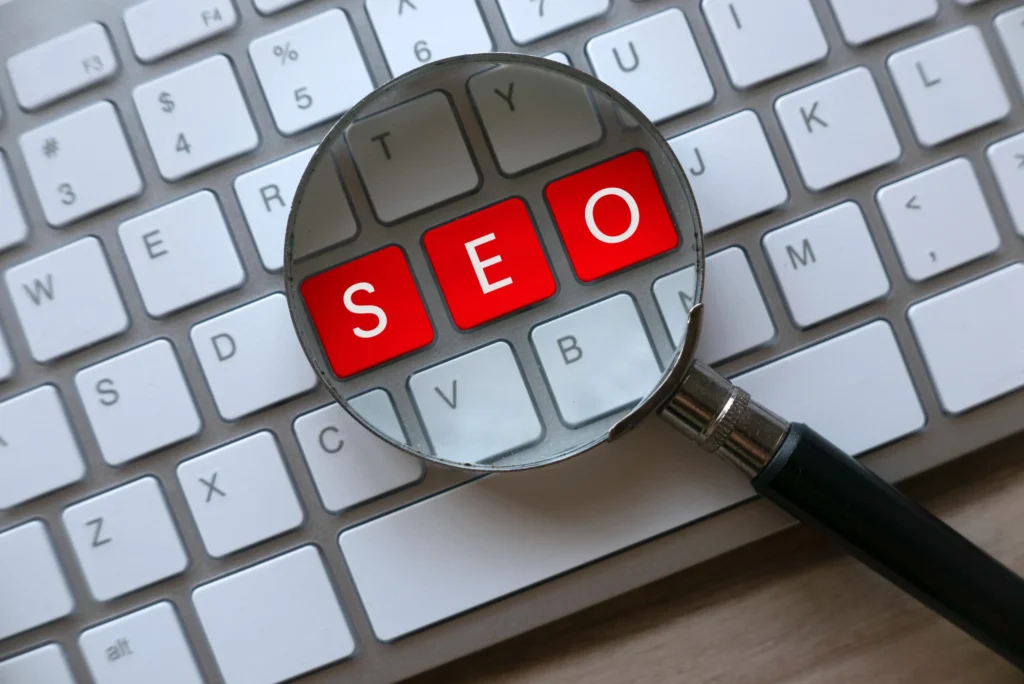 Magnifying glass highlighting the letters SEO on a keyboard during an audit SEO report process.