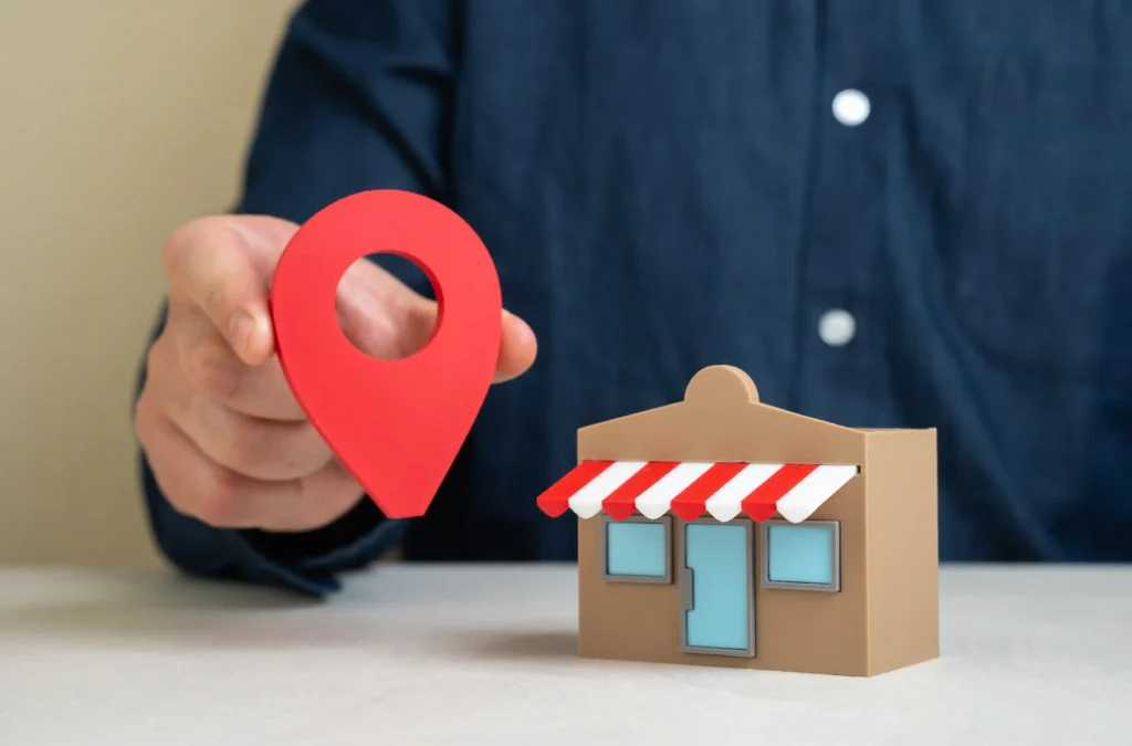 Man holding a red geolocation pin beside a small restaurant model representing local SEO for a food digital marketing agency.