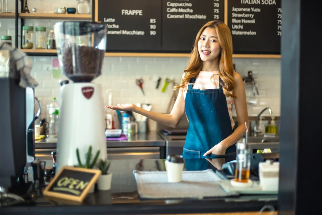 Barista smiling behind the counter presenting a coffee grinder — visual example of coffee marketing ideas in action.