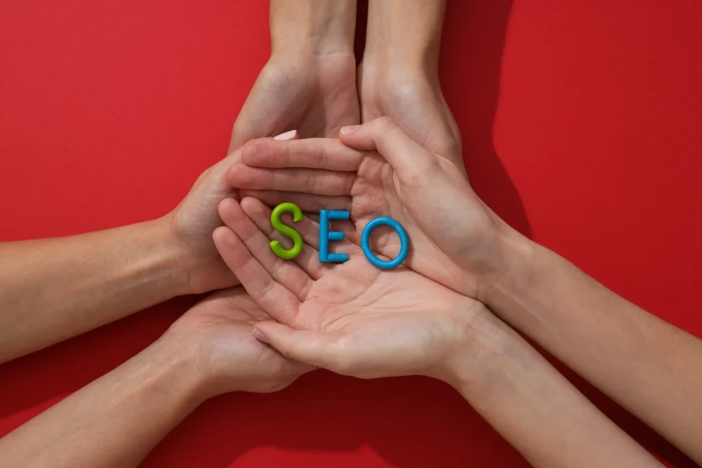 Hands forming a supportive circle holding letters SEO on red background — collaboration by the best agency for local SEO.