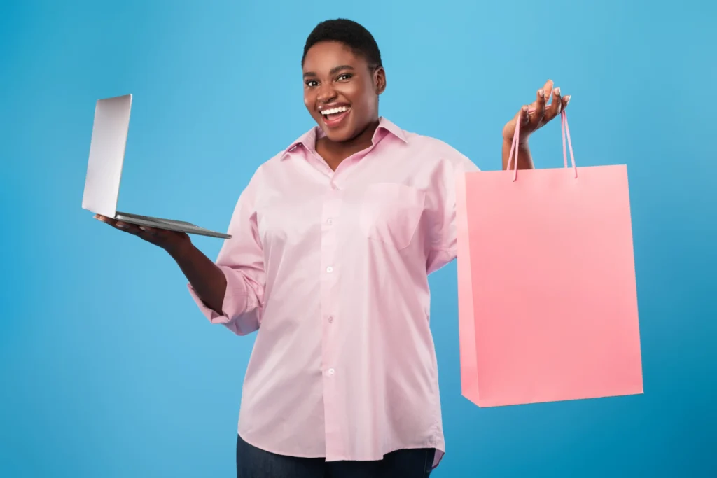 Smiling woman holding a laptop and a pink shopping bag representing online shopping success with an ecommerce branding agency.