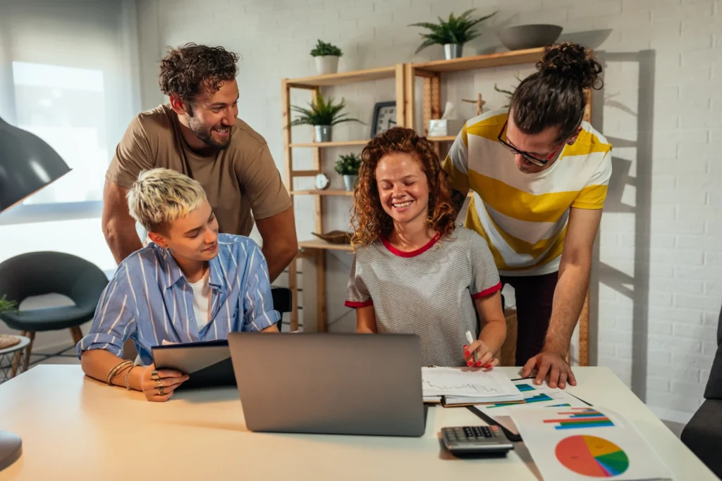 A small digital marketing agency team collaborating around a laptop, reviewing charts and discussing campaign strategies in a bright modern office.