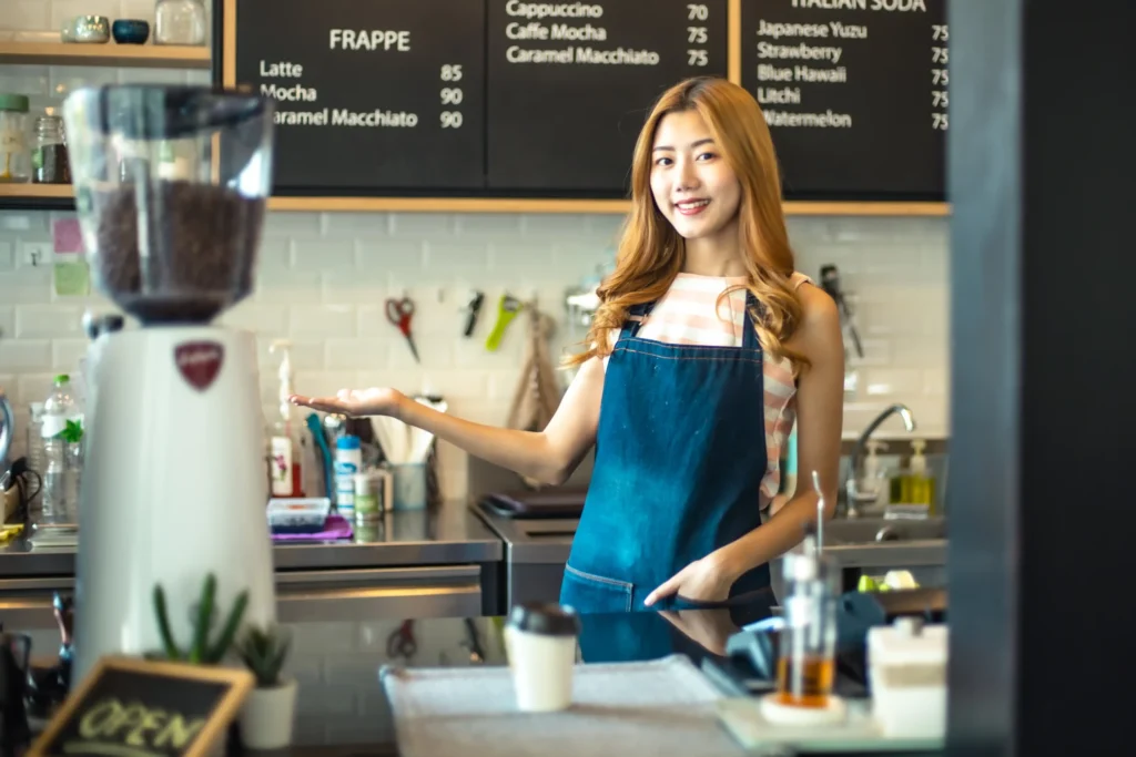 Barista standing behind a café counter, presenting the menu board with confidence and welcoming energy.
