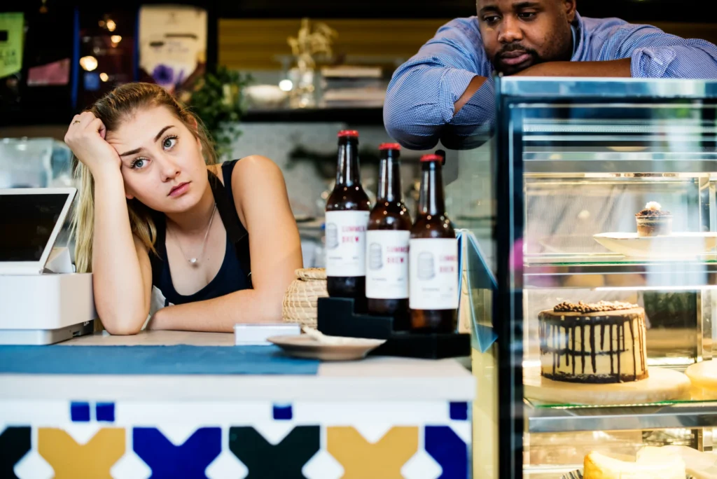 Café owners looking concerned behind the counter with low customer traffic, representing the need for better marketing ideas for cafes.