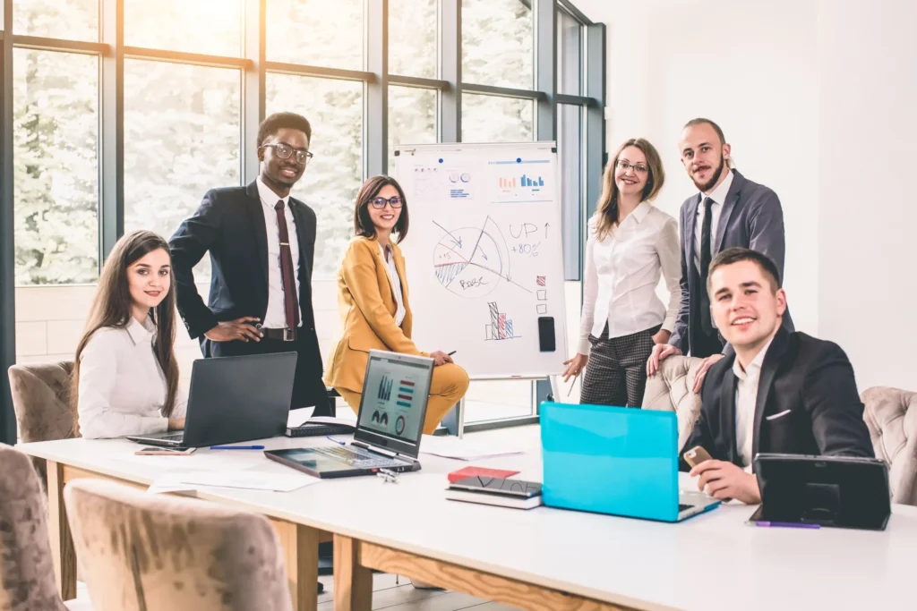 A small digital marketing agency team presenting data and growth metrics on a whiteboard during a strategy meeting with laptops on the table.