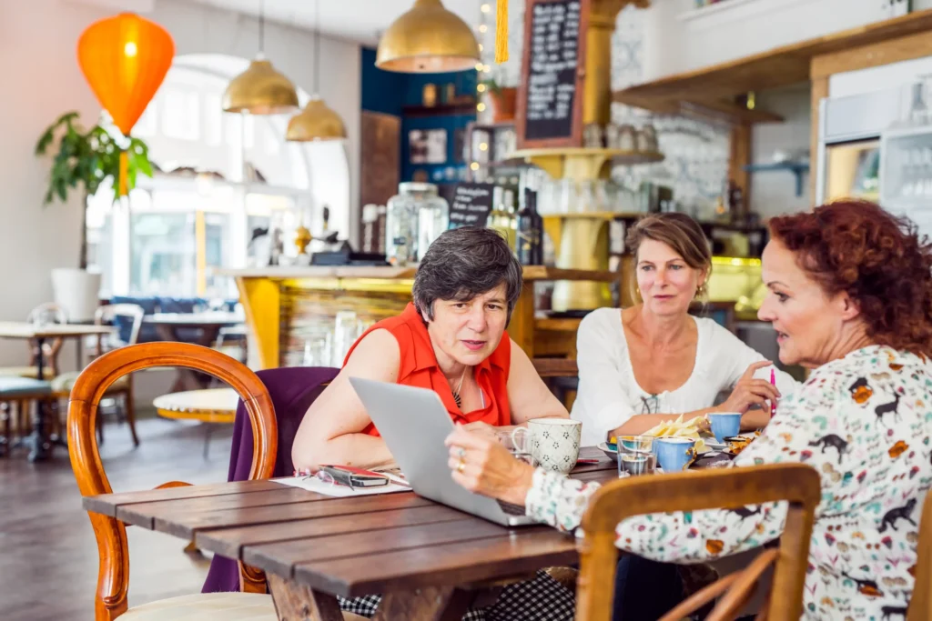 Three women discussing a cafe marketing plan over coffee in a cozy cafe setting.