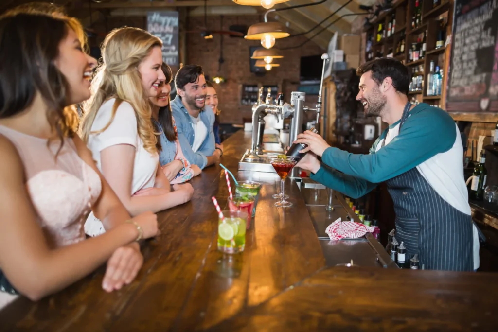 Bartender serving cocktails to happy customers at a lively bar, illustrating social media marketing for bars.