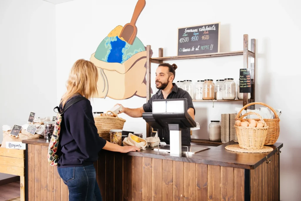 Friendly barista serving a smiling customer at a cozy coffee counter, highlighting welcoming cafe ideas to attract customers.