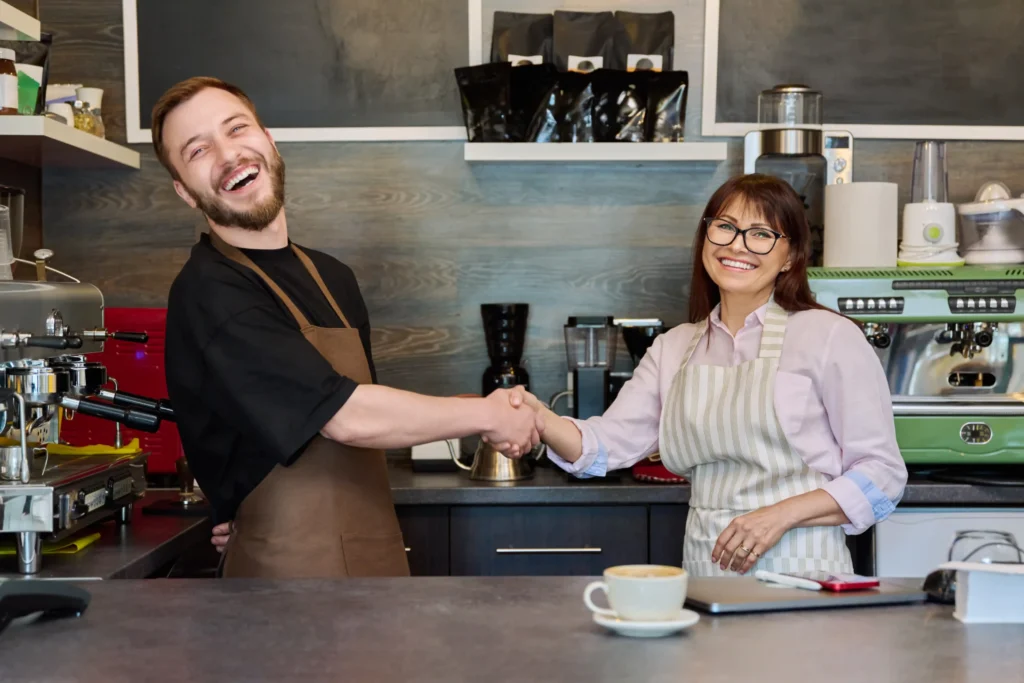 Two café owners shaking hands and smiling, celebrating partnership and growth driven by the local business search engine.