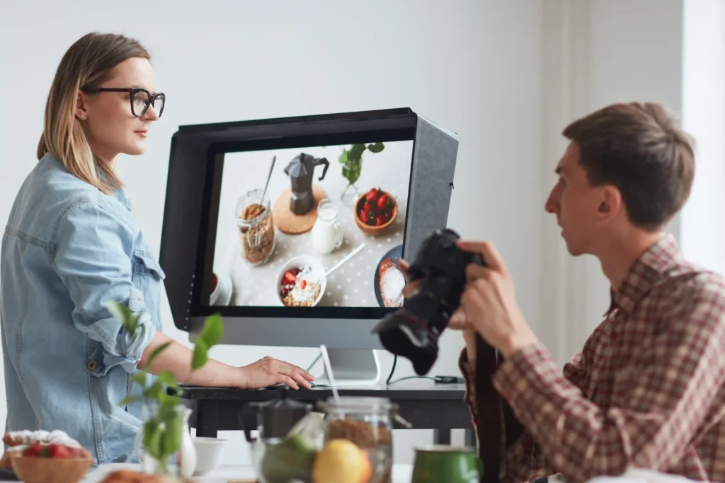 Team of digital marketers reviewing product photos on a monitor during a creative planning session for local search advertising campaigns.