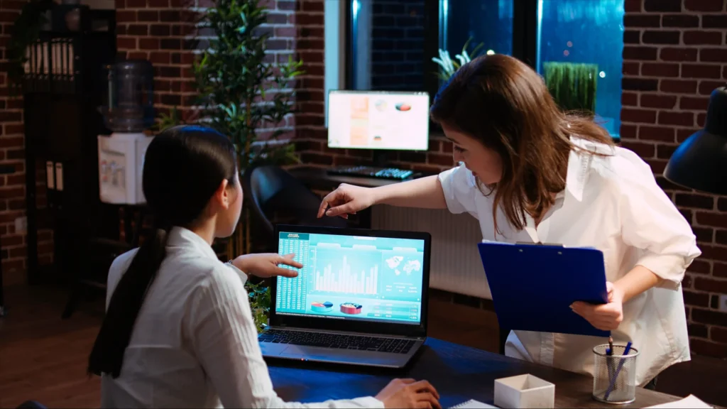 Two team members at a digital media marketing company analyzing performance data on a laptop during a strategy meeting.