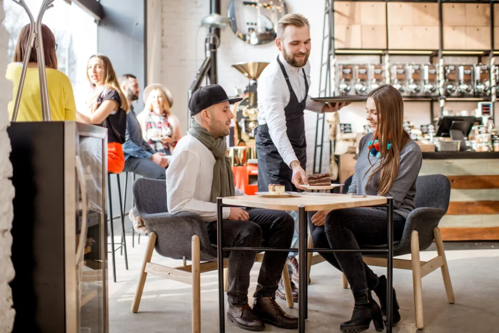 Barista serving desserts to smiling customers inside a cozy café, illustrating real-world cafe promotion ideas in action.