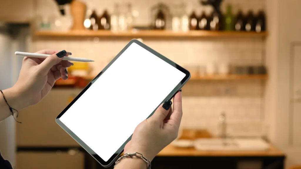 Close-up of a person using a digital tablet in a restaurant setting to plan food and beverage marketing strategy.