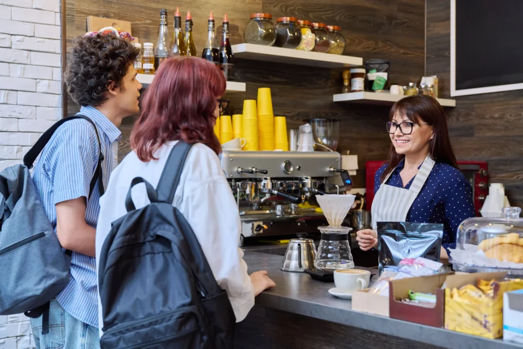 Barista smiling while taking coffee orders from two young customers, representing real-world coffee advertising ideas.