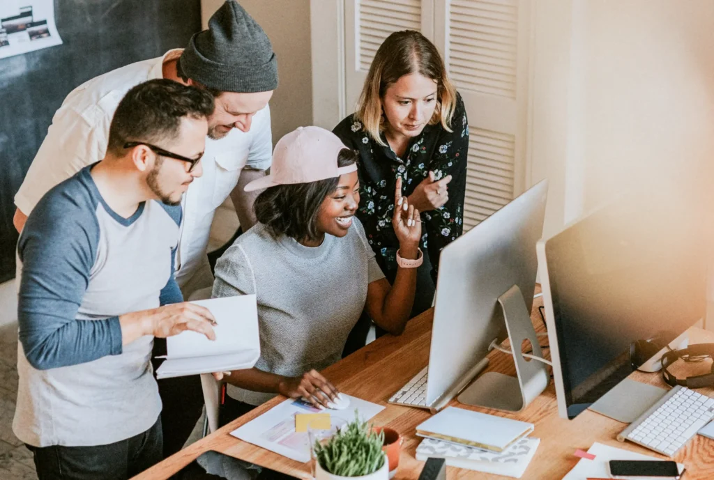 Diverse startup team collaborating around a computer, illustrating teamwork and campaign planning seen in the best performance marketing agencies.