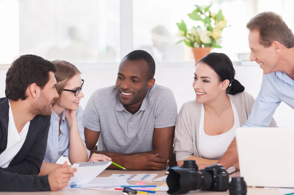 Colleagues smiling and collaborating around a desk while discussing results, representing teamwork within top performance marketing agencies.