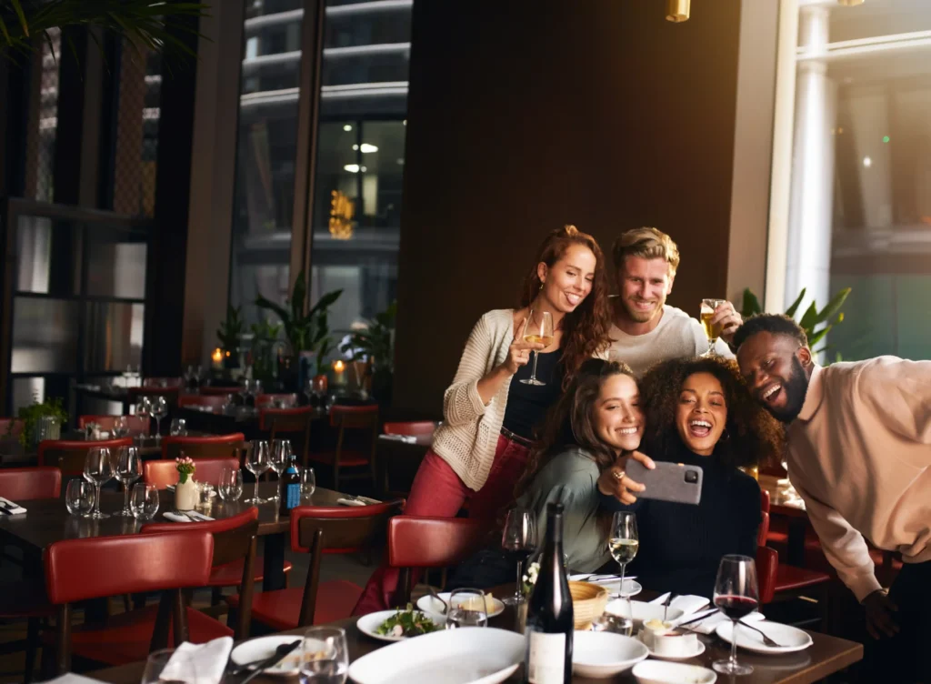 A group of friends taking a selfie at a lively restaurant table, highlighting social engagement and the real-world impact of effective restaurant local SEO strategies.