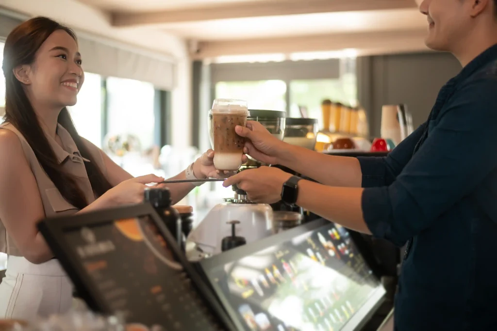 Barista handing an iced coffee to a customer, demonstrating customer experience as part of strong coffee advertising ideas.