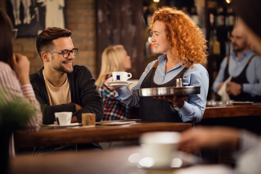 Smiling waitress serving coffee to a guest in a cozy cafe, representing how quality service supports the marketing strategy of a cafe.