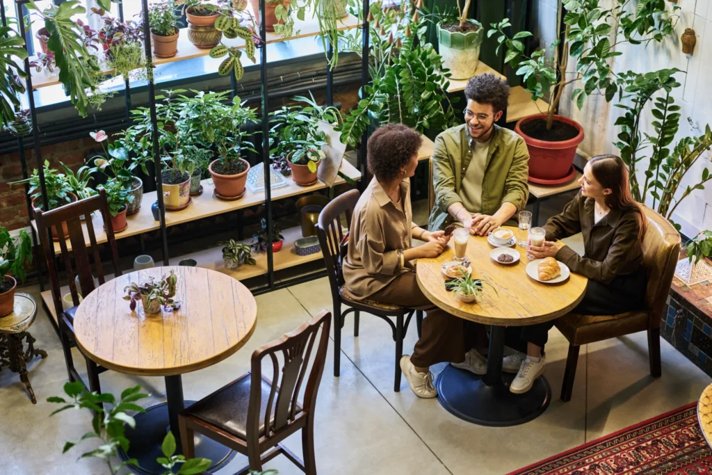 Café customers chatting in a plant-filled coffee shop, reflecting how small businesses can grow with Google Places SEO services.