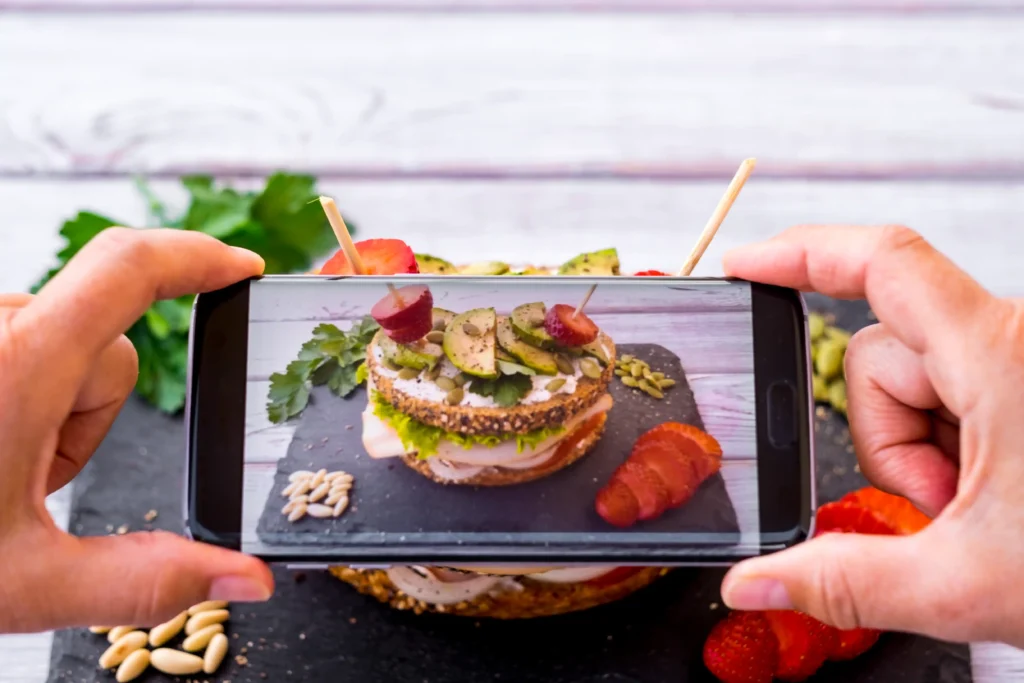 Person photographing a gourmet sandwich for social media as part of a food digital marketing campaign.