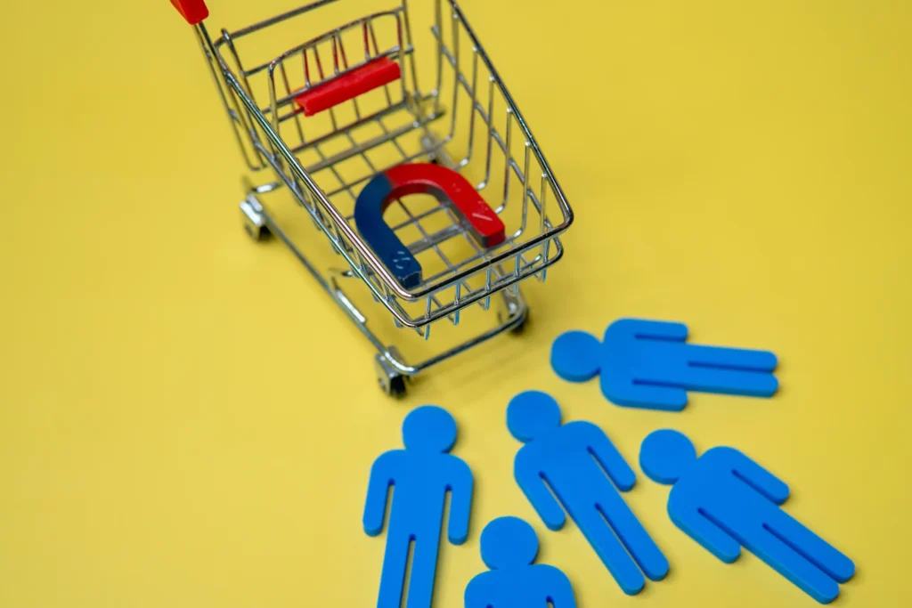 Shopping cart with magnet attracting figures on yellow background, illustrating customer attraction strategies of an ecommerce branding agency.