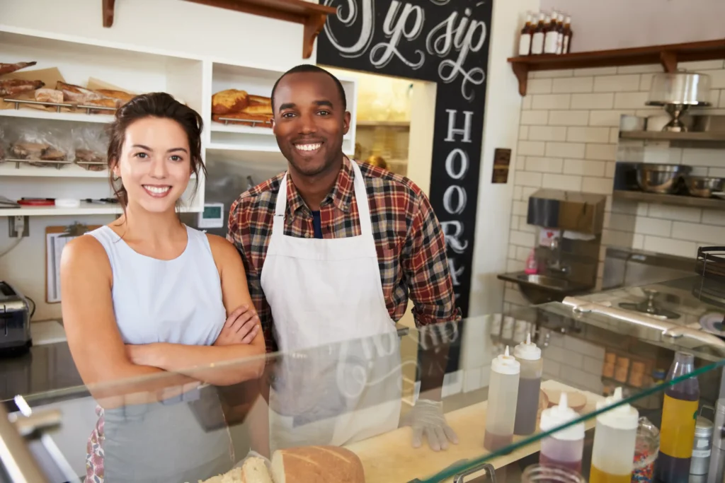 Two deli owners smiling behind the counter, representing businesses gaining exposure through local search optimization services.