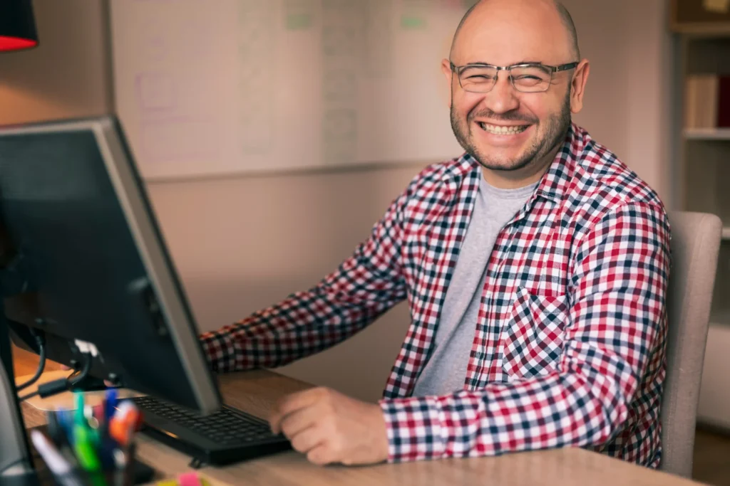 Smiling designer working on digital website design concepts at his desk, reviewing interface ideas and project details.