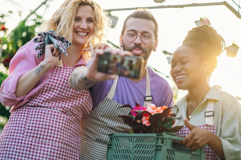 A cheerful group of gardeners taking a selfie in a greenhouse, demonstrating how local search engine marketing services support community-based businesses in reaching local clients.