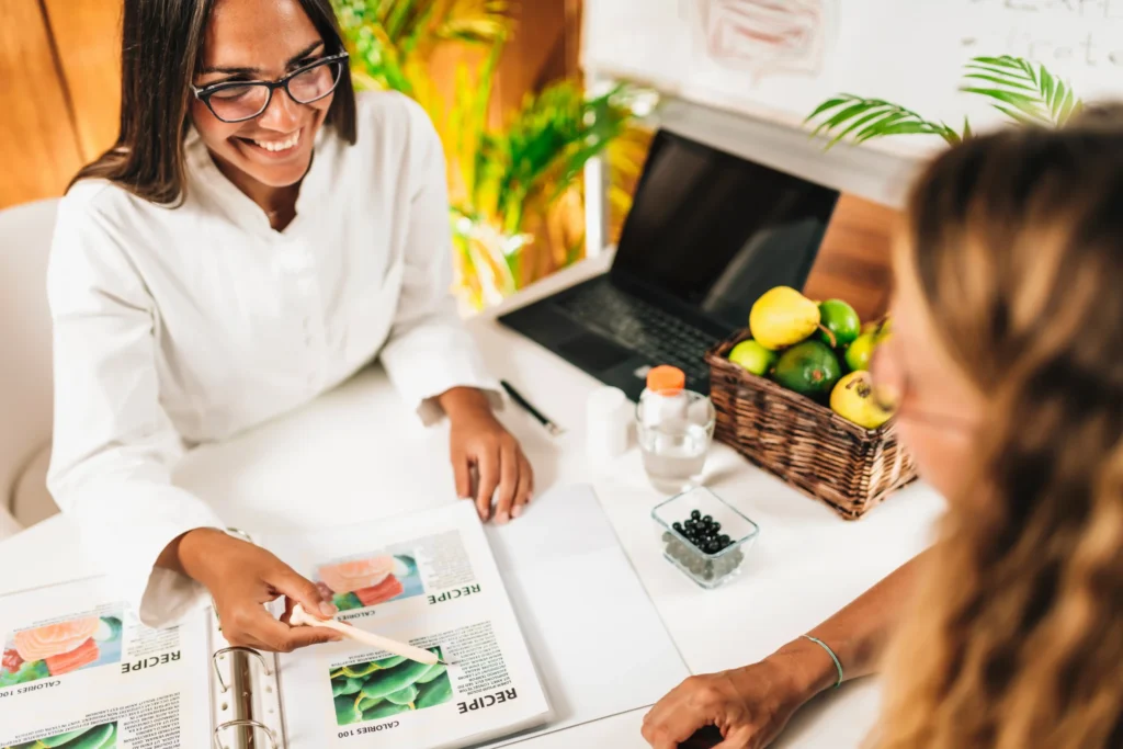 Two women discussing food and menu ideas at a desk, symbolizing local strategy planning by a restaurant marketing agency near me.