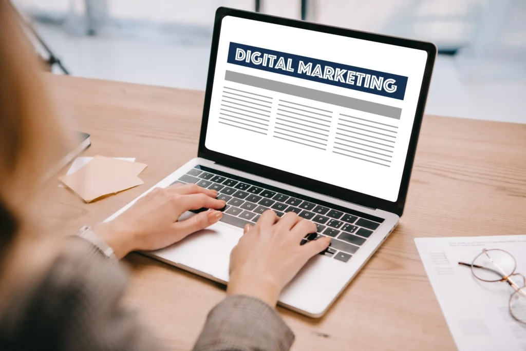 Close-up of hands typing on a laptop with a digital marketing layout on the screen, representing professional digital marketing services involving content writing, SEO, and online strategy.