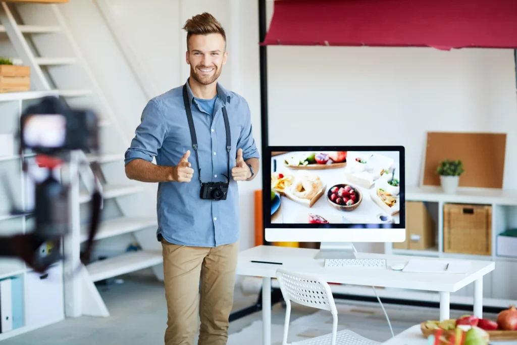 Smiling photographer standing near computer setup with product photos, representing visual branding in local search advertising.