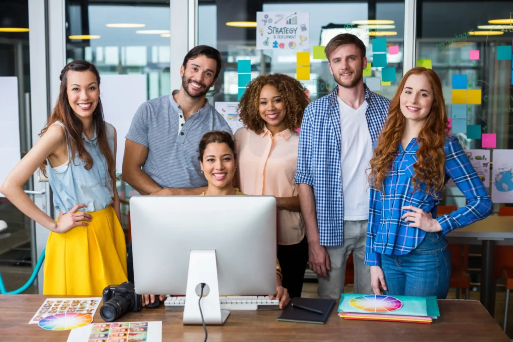 Diverse creative team smiling and collaborating in a design studio, representing teamwork and innovation in an online branding agency.