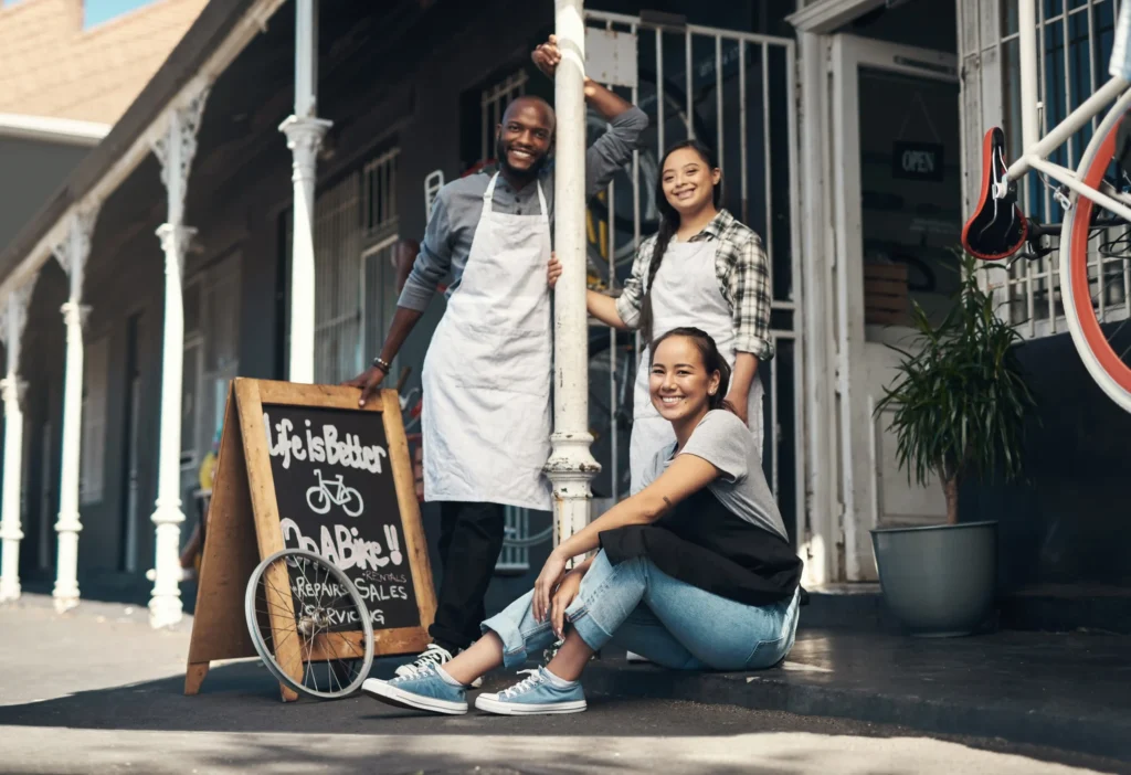 Small business owners posing outside their storefront with a chalkboard sign, illustrating how local search engine marketing services help neighborhood businesses increase foot traffic and customer visibility.