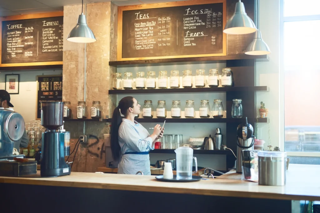 Barista writing updates on café chalkboard menu, illustrating effective visual promotions and coffee advertising ideas.