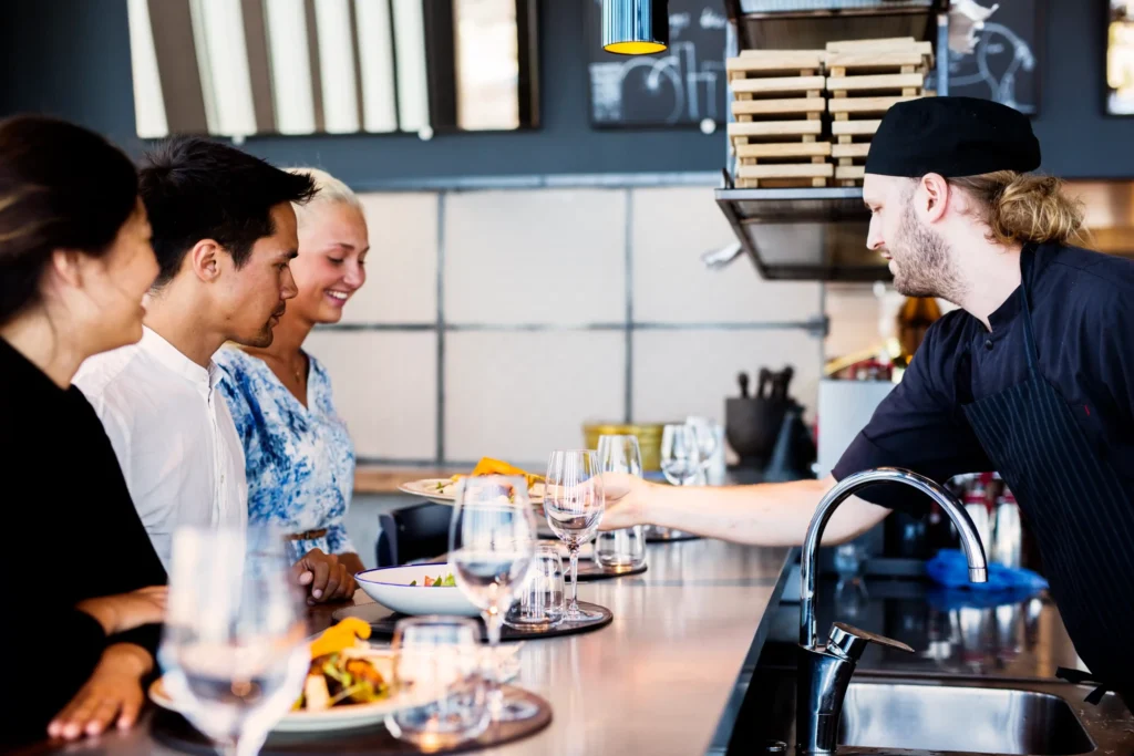 A restaurant chef serving meals to customers at a modern bar counter, symbolizing the customer experience promoted by a social media agency for restaurants.