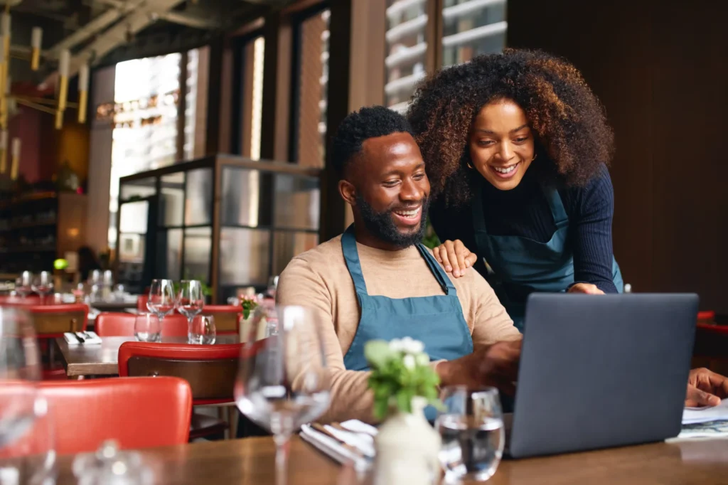 Restaurant owners reviewing online tools on a laptop, demonstrating how marketing services for restaurants support business growth.