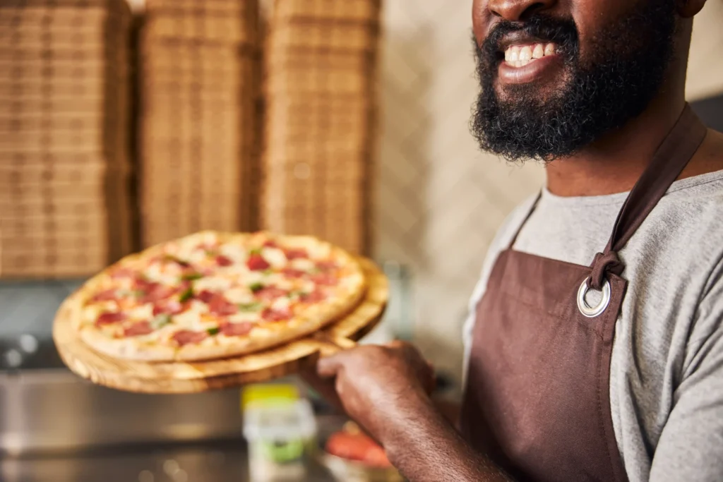 Smiling chef presenting a fresh pizza, illustrating authentic brand storytelling in pizza marketing ideas.