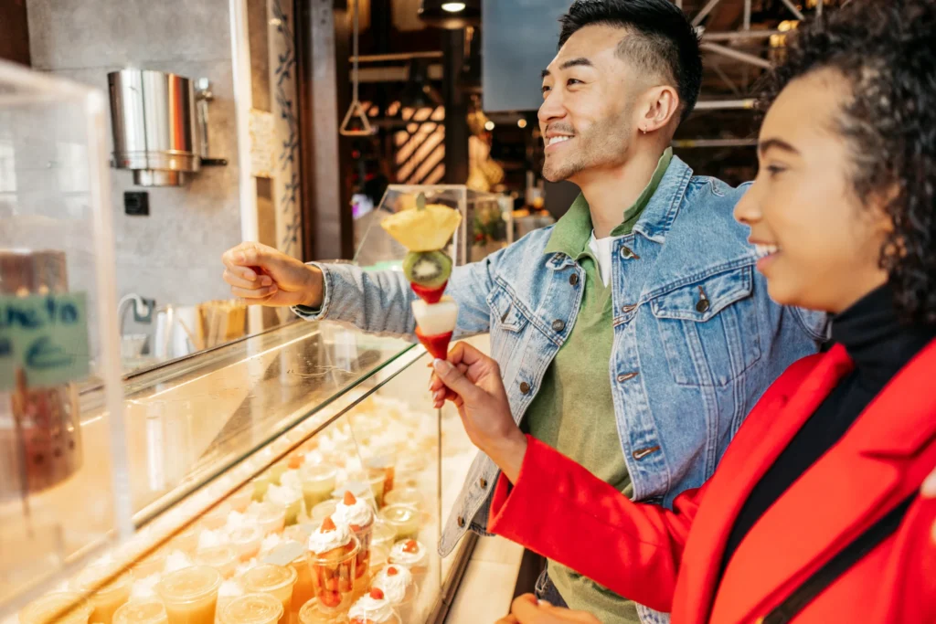 Smiling couple selecting desserts at a shop counter, symbolizing customer experience and retail engagement for food marketing ideas.