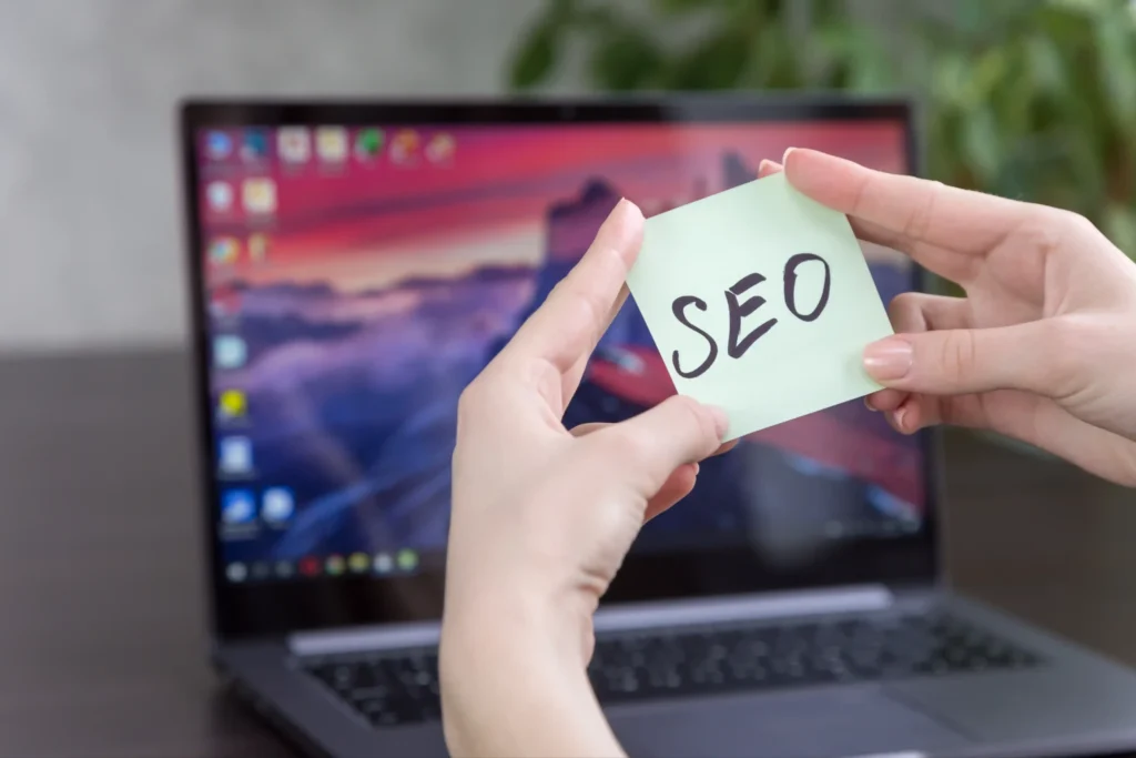 Person holding a sticky note labeled SEO in front of laptop, symbolizing strategy planning for a google maps seo agency.