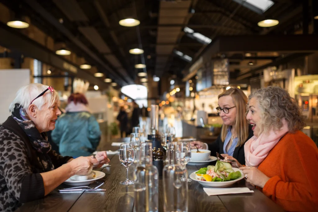 Three women dining and socializing inside a busy restaurant, illustrating customer interaction patterns useful for restaurant market research.